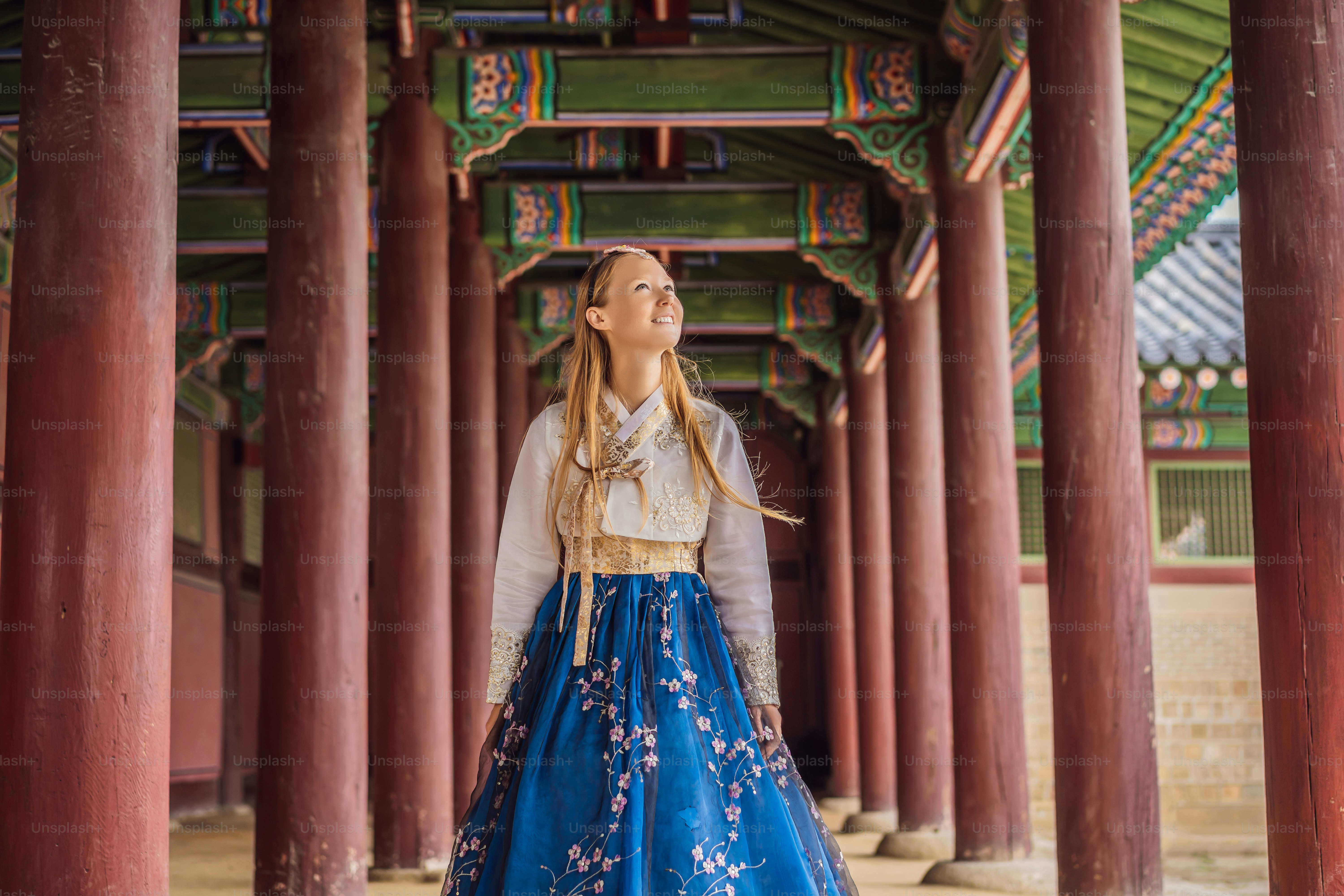 A woman in a traditional blue and white hanbok standing between wooden pillars